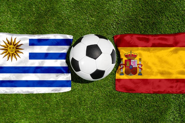 FOTOMONTAGE, Fußball-Weltmeisterschaft 2026: Nationalflaggen von Uruguay und Spanien mit Fußball auf Rasen. Symbolbild zum WM-Gruppenspiel am 27 Juni bei der FIFA Fussball-Weltmeisterschaft 2026