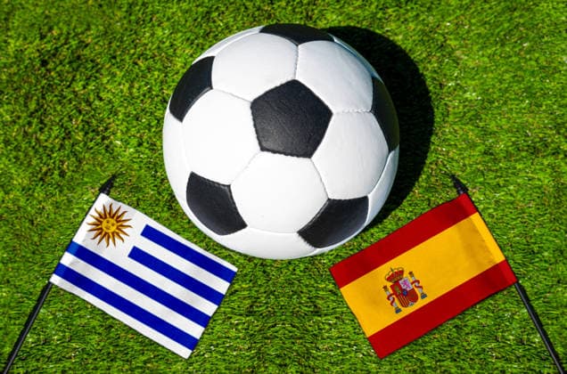 FOTOMONTAGE, Fußball-Weltmeisterschaft 2026: Nationalflaggen von Uruguay und Spanien mit Fußball auf Rasen. Symbolbild zum WM-Gruppenspiel am 27 Juni bei der FIFA Fussball-Weltmeisterschaft 2026
