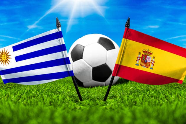 FOTOMONTAGE, Fußball-Weltmeisterschaft 2026: Nationalflaggen von Uruguay und Spanien mit Fußball auf Rasen. Symbolbild zum WM-Gruppenspiel am 27 Juni bei der FIFA Fussball-Weltmeisterschaft 2026