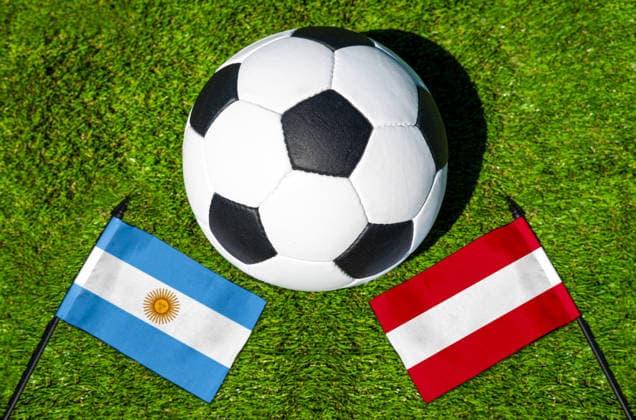 FOTOMONTAGE, Fußball-Weltmeisterschaft 2026: Nationalflaggen von Argentinien und Österreich mit Fußball auf Rasen. Symbolbild zum WM-Gruppenspiel am 22 Juni bei der FIFA Fussball-Weltmeisterschaft 2026