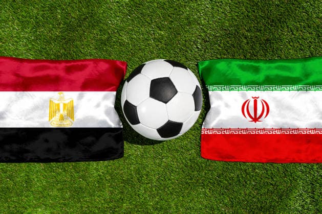 FOTOMONTAGE, Fußball-Weltmeisterschaft 2026: Nationalflaggen von Ägypten und Iran mit Fußball auf Rasen. Symbolbild zum WM-Gruppenspiel am 27 Juni bei der FIFA Fussball-Weltmeisterschaft 2026
