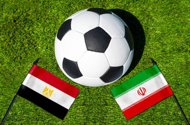 FOTOMONTAGE, Fußball-Weltmeisterschaft 2026: Nationalflaggen von Ägypten und Iran mit Fußball auf Rasen. Symbolbild zum WM-Gruppenspiel am 27 Juni bei der FIFA Fussball-Weltmeisterschaft 2026