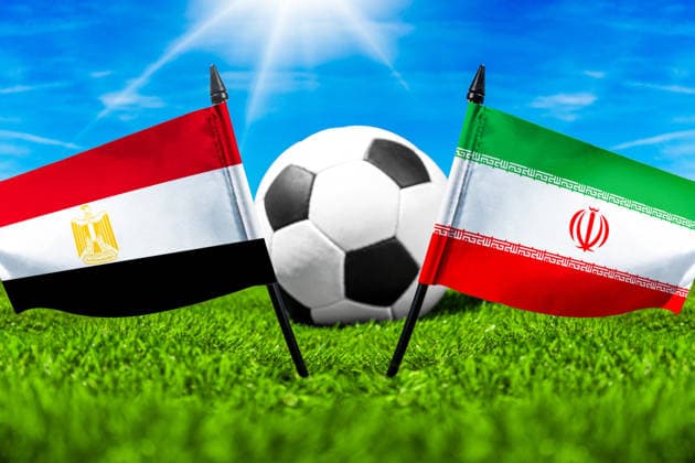 FOTOMONTAGE, Fußball-Weltmeisterschaft 2026: Nationalflaggen von Ägypten und Iran mit Fußball auf Rasen. Symbolbild zum WM-Gruppenspiel am 27 Juni bei der FIFA Fussball-Weltmeisterschaft 2026