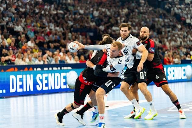 Johannes Golla 3 SG Flensburg Handewitt fights his way through the MT Melsungen defense with the ball, while Adrian Sipos 8 MT Melsungen watches in the background The Melsungen defender with 25 tries to stop Golla MT Melsungen vs SG Flensburg Handewitt - EHF Finals Hamburg 2026 Copyright: xPhilippHeistx