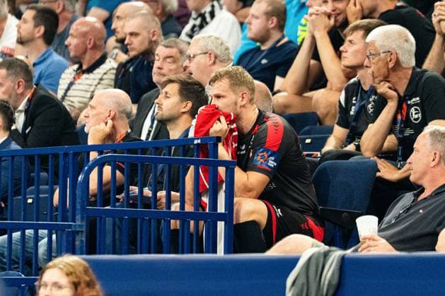 An MT Melsungen player sits on the substitutes bench and watches the game, holding a towel in front of his face Spectators and other people with MT Melsungen accreditations can be seen in the background MT Melsungen vs SG Flensburg Handewitt - EHF Finals Hamburg 2026 Copyright: xPhilippHeistx