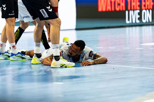 A Montpellier HB player lies flat on the hall floor after a tackle and looks at several SG Flensburg Handewitt players standing around him Montpellier player lies on the hall floor after a tackle Copyright: xPhilippHeistx