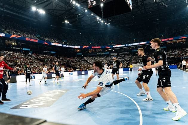 A Montpellier HB player throws himself forward in a drop shot motion during the 3rd Place match, while Domen Novak 63 SG Flensburg Handewitt and another Flensburg player stand in defense The packed arena can be seen in the background with the score 10 on the scoreboard Domen Novak 63 SG Flensburg Handewitt in the match against Montpellier HB Copyright: xPhilippHeistx