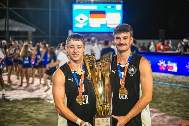 Two players from the German national beach handball team are holding the golden championship trophy together and wearing gold medals around their necks. In the background, the scoreboard with the German flag and celebrating spectators at Lake Jarun in Zagreb can be seen. IHF Beach Handball World Championship 2026, June 23, 2026, Zagreb, Lake Jarun Copyright: xspeedshotx xDorianfrickx