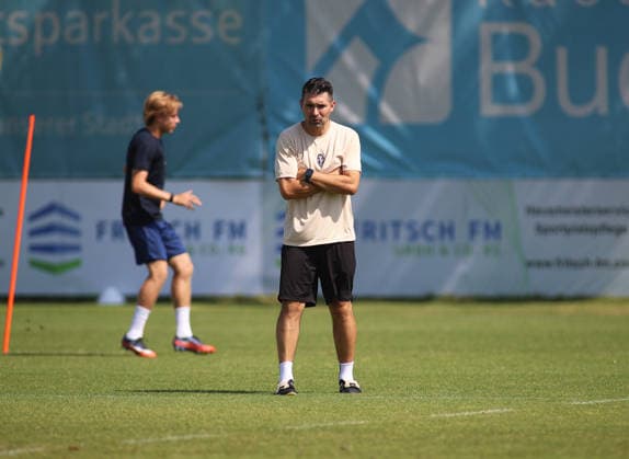 Soccer, Men s, Bavarian Regional League, 2026–2027 Season, TSV 1860 Munich, Alper Kayabunar at practice; TSV 1860 Munich coach standing on the practice field with his arms crossed