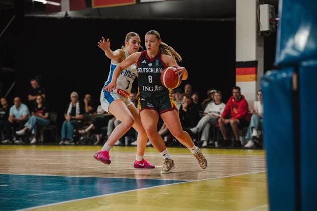 Darina Zraychenko 8 of Germany drives the ball past a Finnish defender in a one-on-one situation toward the basket. Spectators and a German flag can be seen in the background. Darina Zraychenko 8 of Germany dribbling against Finland Copyright: xJoelxKruehlerx