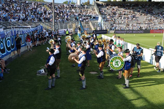 Soccer, Men s, Bavarian Regional League, 2026–2027 Season, TSV 1860 Munich vs. FC Augsburg II, Grünwalder Stadium: The Sechzger Musikanten, a brass band affiliated with TSV 1860 Munich, performing in front of the West Stand