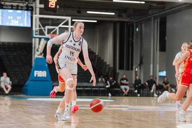 Frederike Askamp 14 of Germany dribbles the ball toward the basket, while a Montenegrin player runs alongside her on the right edge of the frame. In the background, the court at Kistamässan in Stockholm is visible. Frederike Askamp 14 of Germany drives the ball forward Copyright: xJoelxKruehlerx