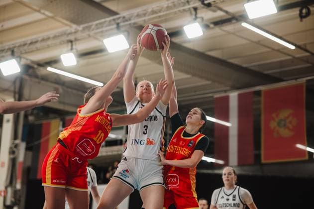 Greta Metz (No. 3, Germany) is bracing herself with both hands against two Montenegrin players, including No. 10 Anja Adzic, to maintain possession of the ball. In the background, Lara Gierlich (No. 12, Germany) can be seen watching the action. Greta Metz (No. 3, Germany) is battling for the ball against Montenegro. Copyright: xJoelxKruehlerx