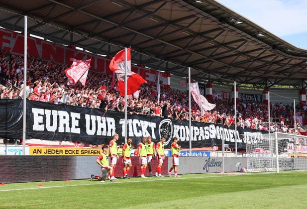 Hall S, August 9, 2026, Leuna Chemie Stadium, Regional League Northeast, Matchday 4, HALLESCHER FC vs. CHEMNITZER FC 0–0. Pictured: Hallescher FC fans chanting COMPASS MODEL NOW—YOUR CLOCK IS TICKING, Picture Point