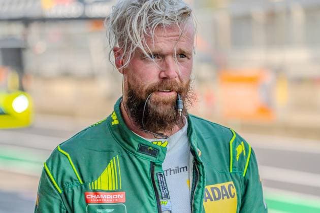 Nicki Thiim of Comtoyou Racing stands in the pit lane at the Nürburgring wearing his green-and-neon-yellow racing suit and headset. The Champion Lubricants and ADAC logos are visible on the suit. A portrait of Nicki Thiim of Comtoyou Racing at the Nürburgring Copyright: xMichaelxSchäferx