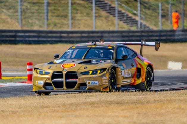 The Schubert Motorsport BMW M4 GT3 No. 3, with Kelvin van der Linde at the wheel, navigates a turn at the Nürburgring. The car features a special gold Shell Helix paint scheme with red accents, orange, and green. Kelvin van der Linde’s BMW M4 GT3 3 from Schubert Motorsport at the Nürburgring Copyright: xMichaelxSchäferx