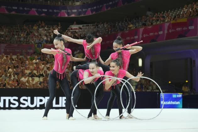 The Kazakhstani team performs a synchronized group routine with hoops and clubs at the Festhalle in Frankfurt. The five gymnasts in pink leotards form a dynamic formation in front of a full house. Kazakhstan during the group routine with hoops and clubs Copyright: xspeedshotx