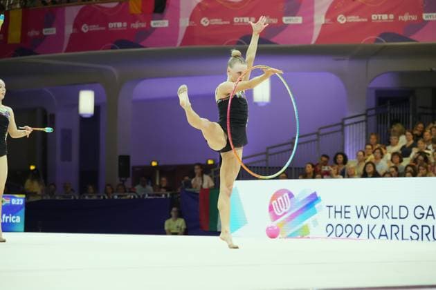 A gymnast performs a hoop routine featuring a high-leg balance element at the Festhalle in Frankfurt. In the background, another athlete can be seen performing with clubs. A gymnast with a hoop at the Rhythmic Gymnastics World Championships in Frankfurt Copyright: xspeedshotx