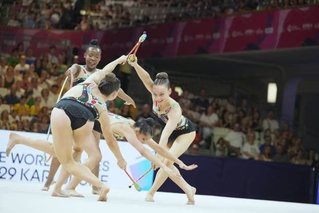 A group of gymnasts performs a synchronized clubs routine at the Festhalle in Frankfurt. The athletes move in tight formation, while the packed audience in the background frames the scene. Group clubs routine at the 2026 Rhythmic Gymnastics World Championships Copyright: xspeedshotx