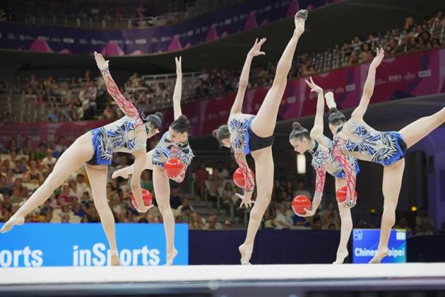 Five gymnasts from a group perform a synchronized ball routine in Frankfurt s Festhalle, their legs stretched high in the air and the red balls in flight. In the background, the packed audience can be seen against the pink World Championships backdrop. Group routine with balls at the Rhythmic Gymnastics World Championships in Frankfurt Copyright: xspeedshotx