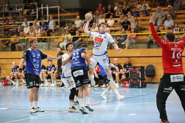 Alexander Hartwig, 24, of VfL Lübeck Schwartau, rises for a jump shot at the Hansehalle in Lübeck, while Rune Overlund (25, Grindstedt GIF) and other Grindstedt GIF defenders guard him from below. On the right side of the picture, Christian Wetche (16, Grindstedt GIF) is positioned as the goalkeeper as Alexander Hartwig (24, VfL Lübeck Schwartau) attempts a jump shot against Grindstedt GIF. Copyright: xspeedshotx