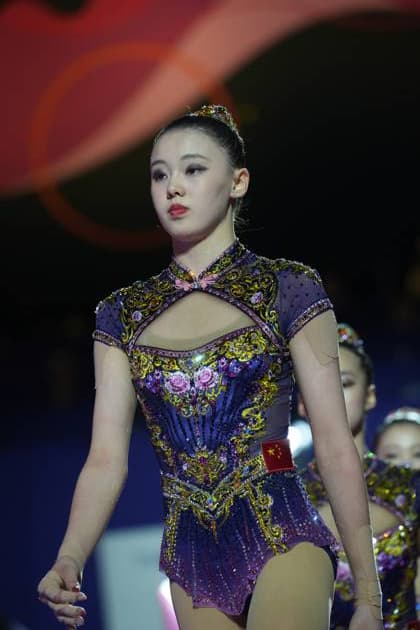 A gymnast from the Chinese team stands in her elaborately embroidered and rhinestone-embellished competition leotard in the Festhalle Frankfurt. The Chinese national emblem is clearly visible on the leotard. Chinese gymnast at the 2026 Rhythmic Gymnastics World Championships in Frankfurt Copyright: xspeedshotx