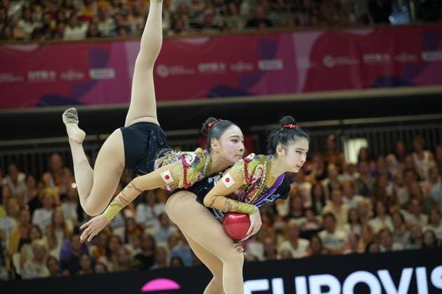 Three gymnasts from the Japanese national team perform a synchronized group routine with a ball at the 2026 Rhythmic Gymnastics World Championships in Frankfurt am Main. One gymnast stretches her leg high into the air, while two others hold the red ball together, with the packed audience at Frankfurt’s Festhalle visible in the background. The Japanese group team performs a group routine with a ball at Frankfurt’s Festhalle. Copyright: xspeedshotx