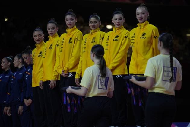 The Brazilian group team CBG stands in yellow training jackets at the medal ceremony for the Rhythmic Gymnastics World Championships in Frankfurt’s Festhalle. Two volunteers in light yellow T-shirts present the medals on trays in front of the athletes. Brazilian group at the medal ceremony for the Rhythmic2026 Rhythmic Gymnastics World Championships Copyright: xspeedshotx