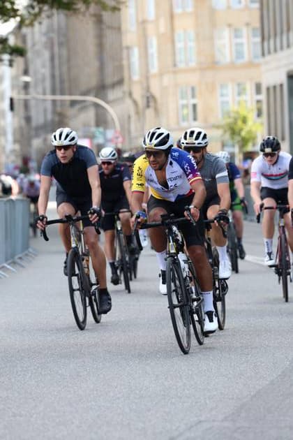 A group of cyclists rides in tight formation through the streets of Hamburg near Rathausmarkt. In the foreground is a rider in the yellow-and-white INEOS jersey, flanked by other riders. The peloton at the EuroEyes Cyclassics in Hamburg Copyright: xspeedshotx xSarahxWolfx