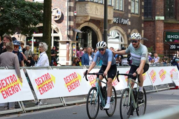 Two cyclists pass the Dextro Energy barrier at Hamburg s Rathausmarkt during the Cyclassics race. In the background, numerous spectators watch the race against a historic backdrop. Two cyclists at the Cyclassics Hamburg at Rathausmarkt Copyright: xspeedshotx xSarahxWolfx