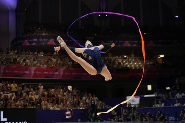 Darja Varfolomeev performs a long jump with a ribbon at the Festhalle in Frankfurt, the colorful ribbon traces an elegant curve through the air. In the background, the packed stands of the 2026 World Championships in Rhythmic Gymnastics can be seen. Darja Varfolomeev performing a jump with the ribbon at the Rhythmic Gymnastics World Championships in Frankfurt Copyright: xspeedshotx