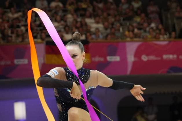 Darja Varfolomeev performs a ribbon routine at the 2026 Rhythmic Gymnastics World Championships in Frankfurt’s Festhalle. The orange-pink ribbon traces an elegant curve across the frame, while the athlete performs with a focused demeanor. 2026 Rhythmic Gymnastics World Championships: Gymnast with a ribbon at the Festhalle Frankfurt Copyright: xspeedshotx