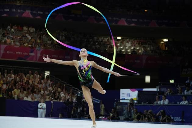 A gymnast performs an elegant balancing routine with a colorful ribbon at the 2026 Rhythmic Gymnastics World Championships in Frankfurt’s Festhalle. The rainbow-colored ribbon forms a large loop above her, while she balances on one leg and spreads her arms wide. 2026 Rhythmic Gymnastics World Championships – Gymnast with a ribbon at the Festhalle in Frankfurt Copyright: xspeedshotx