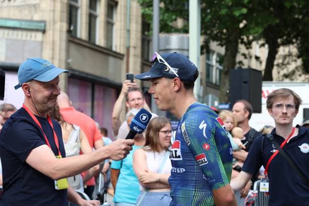 Paul Magnier of Soudal Quick-Step gives an interview to an NDR reporter at Hamburg s Rathausmarkt. In the background, numerous spectators watch the scene of Paul Magnier of Soudal Quick-Step being interviewed by NDR at the Cyclassics Hamburg. Copyright: xspeedshotx xSarahxWolfx