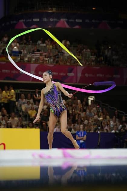 A gymnast from the U.S. performs a ribbon routine at the 2026 World Championships in Rhythmic Gymnastics at the Festhalle in Frankfurt. The colorful ribbon forms a wide loop above her head as she balances on one leg. Rhythmic gymnastics ribbon routine at the World Championships in Frankfurt Copyright: xspeedshotx