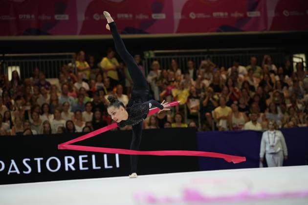 Mariia Borisova performs a ribbon routine in an extreme backbend with her leg extended vertically. In the background, a packed audience watches the 2026 Rhythmic Gymnastics World Championships in Frankfurt am Main. Mariia Borisova performs her ribbon routine at the Festhalle Frankfurt. Copyright: xspeedshotx