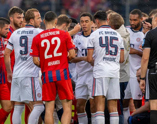August 18, 2026, 2026–2027 Bundesliga, Friendly Match, 1. FC Heidenheim vs. FC Bayern Munich, at the Voith Arena in Heidenheim; after collapsing again during the game, Jamal Musiala (center), of Bayern Munich, is treated by team doctor Prof. Dr. Peter Ueblacker and then led off the field; players from both teams stand around him, concerned; Harry Kane (left), FC Bayern Munich, strokes his cheek comfortingly