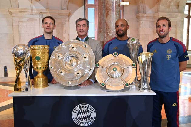 From left: Manuel NEUER, goalkeeper for Bayern Munich; Markus SOEDER, Minister-President of Bavaria and CSU Chairman; Coach Vincent KOMPANY of Bayern Munich; and Harry KANE of Bayern Munich stand behind the trophies, cups, and awards won during the 2025–26 season,Championship Trophy, DFB Cup, and Super Cup. Markus SÖDER, Minister-President of Bavaria and CSU Chairman, welcomes the championship teams of FC Bayern Munich to the Kuppelsaal in the State Chancellery in Munich on September 16, 2026.