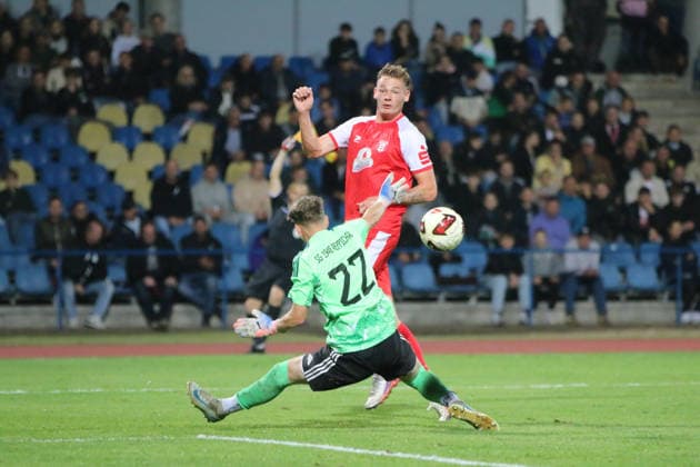 October 2, 2026 Men s Soccer 2026–2027 dachbleche24 State Cup, 2nd Round: SG Reppichau vs. Hallescher FC at Paul Greifzu Stadium, Dessau-Roßlau; Lucas Ehrlich, Halle, 18, in red, passes the ball from an offside position past Niels De Wispelaere of Reppichau, 22, in green, at the Dessau-Roßlau Stadium in Saxony-Anhalt, Germany