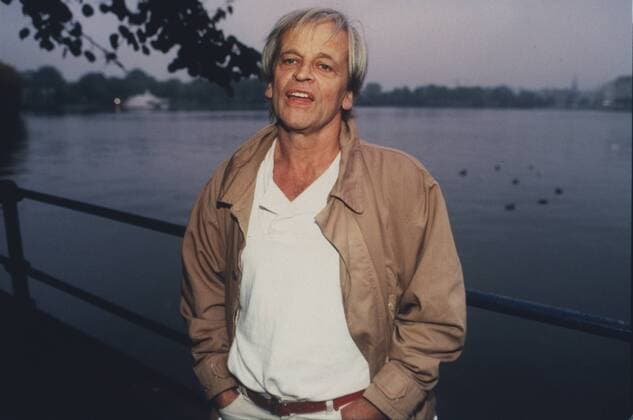 Klaus Kinski (Schauspieler) 10 85 vZ Mann TV Fernsehen Schauspiel Film Kino grauhaarig leger Jacke Hemd stehend draußen Wasser Fluß Geländer Ufer Park Baum halb quer neutral Farbnegativ Internegativ von Bild Nummer 372201