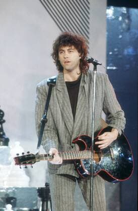 Bob Geldof (Sänger) 11 86 vZ Bob Geldof am 21.11.1986 in Peters Pop Show , ZDF - Sendedatum 6.12.1986 Irland Ire irischer Mann Popmusik Pop Rockmusik Rock Musik Musiker Instrument Texter Komponist TV Fernsehen Sänger Musiksendung irish man musician singer songwriter Bühne Gitarre haltend spielend singend stehend neutral Anzug dunkelhaarig lockig Locken halb hoch