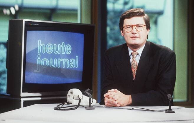 Sigmund Gottlieb 09 89 ru Mann Journalismus Moderation News Brille dunkelhaarig seriös Sakko Krawatte quer halb sitzend Studio Logo Telefon Hände neutral