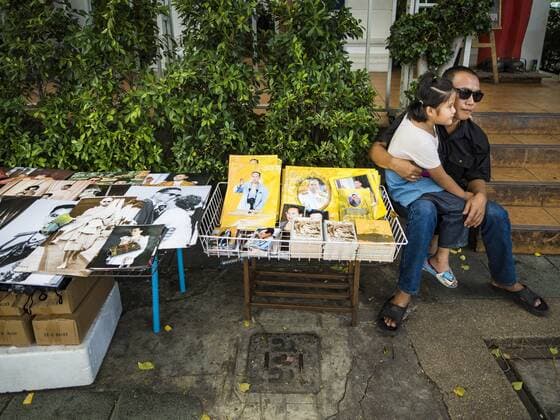 October 15, 2016 - Bangkok, Bangkok, Thailand - A vendor, with his daughter on his knee, sells portraits of Bhumibol Adulyadej, the King of Thailand, near the Grand Palace in Bangkok. King Bhumibol Adulyadej died Oct. 13, 2016. He was 88. His death comes after a period of failing health. With the king s death, the world s longest-reigning monarch is Queen Elizabeth II, who ascended to the British throne in 1952. Bhumibol Adulyadej, was born in Cambridge, MA, on 5 December 1927. He was the ninth monarch of Thailand from the Chakri Dynasty and is known as Rama IX. He became King on June 9, 1946 and served as King of Thailand for 70 years, 126 days. He was, at the time of his death, the world s longest-serving head of state and the longest-reigning monarch in Thai history. Bangkok Thailand - ZUMAk94_