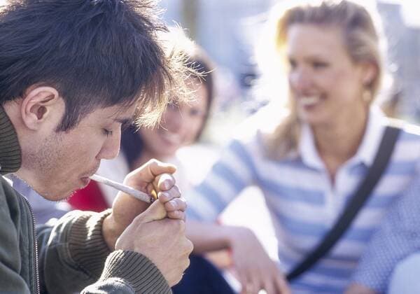 Junger Mann zuendet sich einen Joint an, Frauen im Hintergrund (model-released) Copyright: xMEVx ALLMVMEV60014