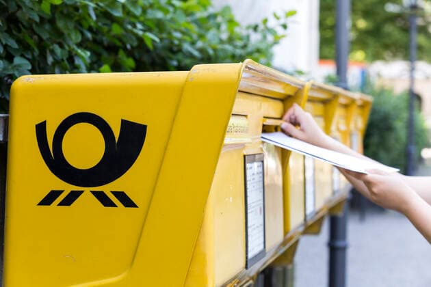 Woman puts several letters into a mailbox of the Deutsche Post AG