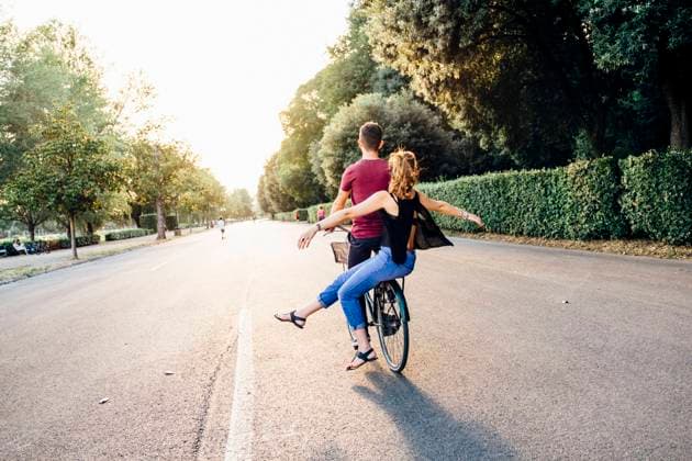Young woman with arms outstretched sitting with boyfriend on bicycle in park model released Symbolfoto SBAF00032