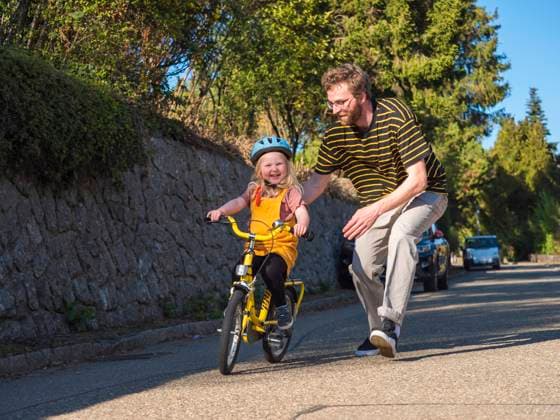 IMAGO Creative: Vaterschaft Father supporting daughter while cycling on road model released Symbolfoto LAF02713