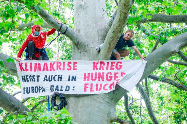 Climate activists occupy Monbijou Park Germany, Berlin on 16 08 2021 Two climate activists with climbing rope high on a tree They display a banner Climate crisis means soon war hunger flight also in Europe