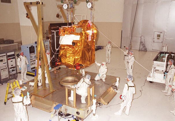 In the Spacecraft Assembly & Encapsulation Facility -2, workers help guide the <a href=http: mars.jpl.nasa.gov 2001 >2001 Mars Odyssey Orbiter < a>as it is lowered to a workstand. The Mars Odyssey Orbiter carries three science instruments: the Thermal Emission Imaging System (THEMIS), the Gamma Ray Spectrometer (GRS), and the Mars Radiation Environment Experiment (MARIE). THEMIS will map the mineralogy and morphology of the Martian surface using a high-resolution camera and a thermal infrared imaging spectrometer. The GRS will achieve global mapping of the elemental composition of the surface and determine the abundance of hydrogen in the shallow subsurface. The GRS is a rebuild of the instrument lost with the Mars Observer mission. The Copyright: xpiemagsx piemagsspace-16295 !ACHTUNG AUFNAHMEDATUM GESCHÄTZT!