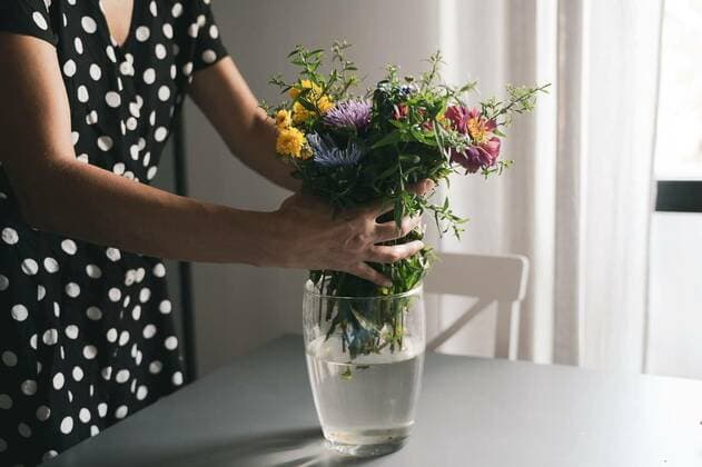 woman arranging a bouquet of flowers in a glass vase, young Caucasian woman with black dress and white polka dots arranging a bouquet of freshly picked up beautiful flowers in a glass vase on a grey table in natural day light model released, Symbolfoto , 17.03.2021, Copyright: xmacondox Panthermedia29710378.jpg